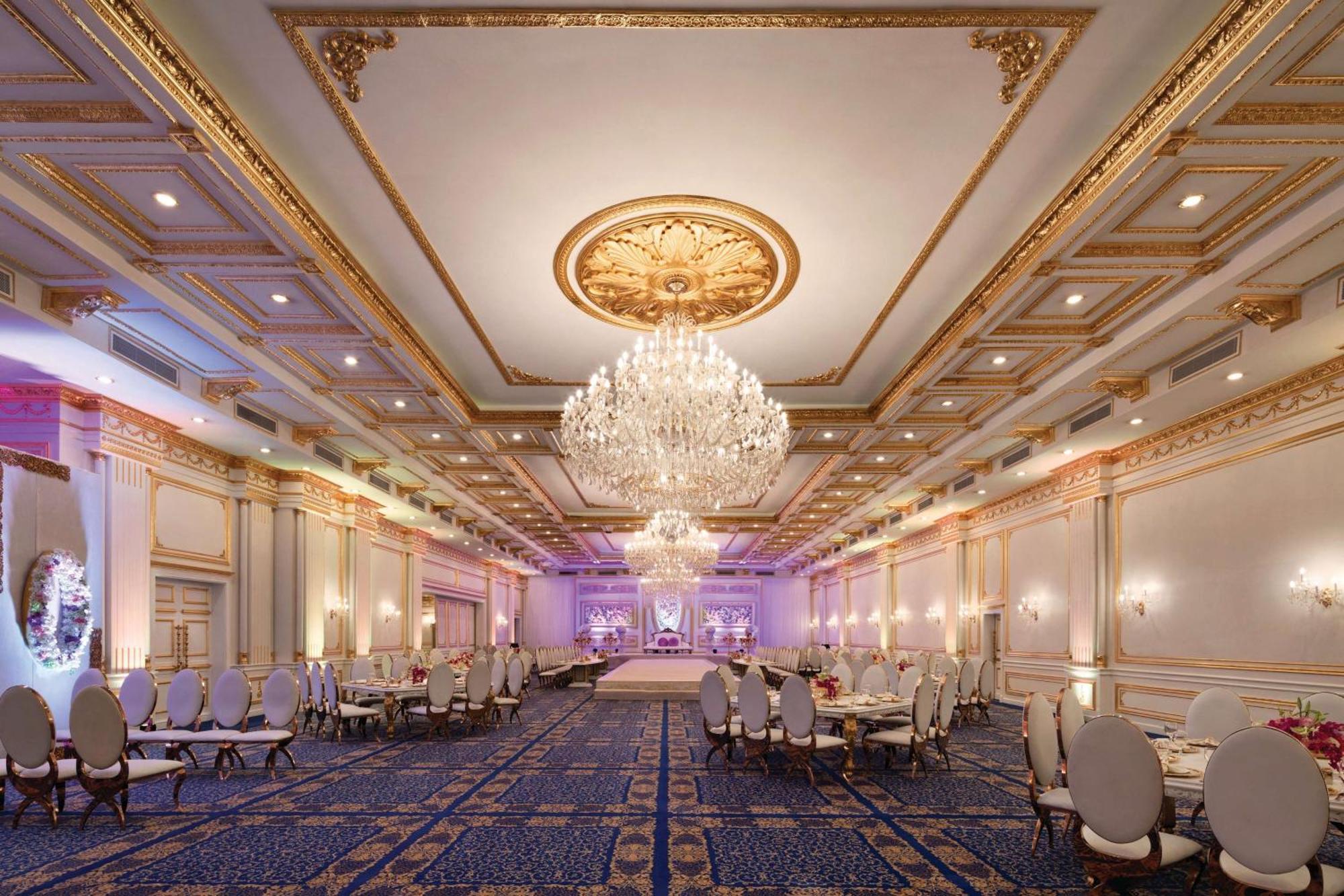 Grand Regency Doha, Trademark Collection By Wyndham Екстериор снимка The photo shows an elegant banquet hall with luxurious decor. The room features high ceilings adorned with intricate gold details and a large chandelier that hangs in the center, providing soft illumination. There are several round tables with plush 