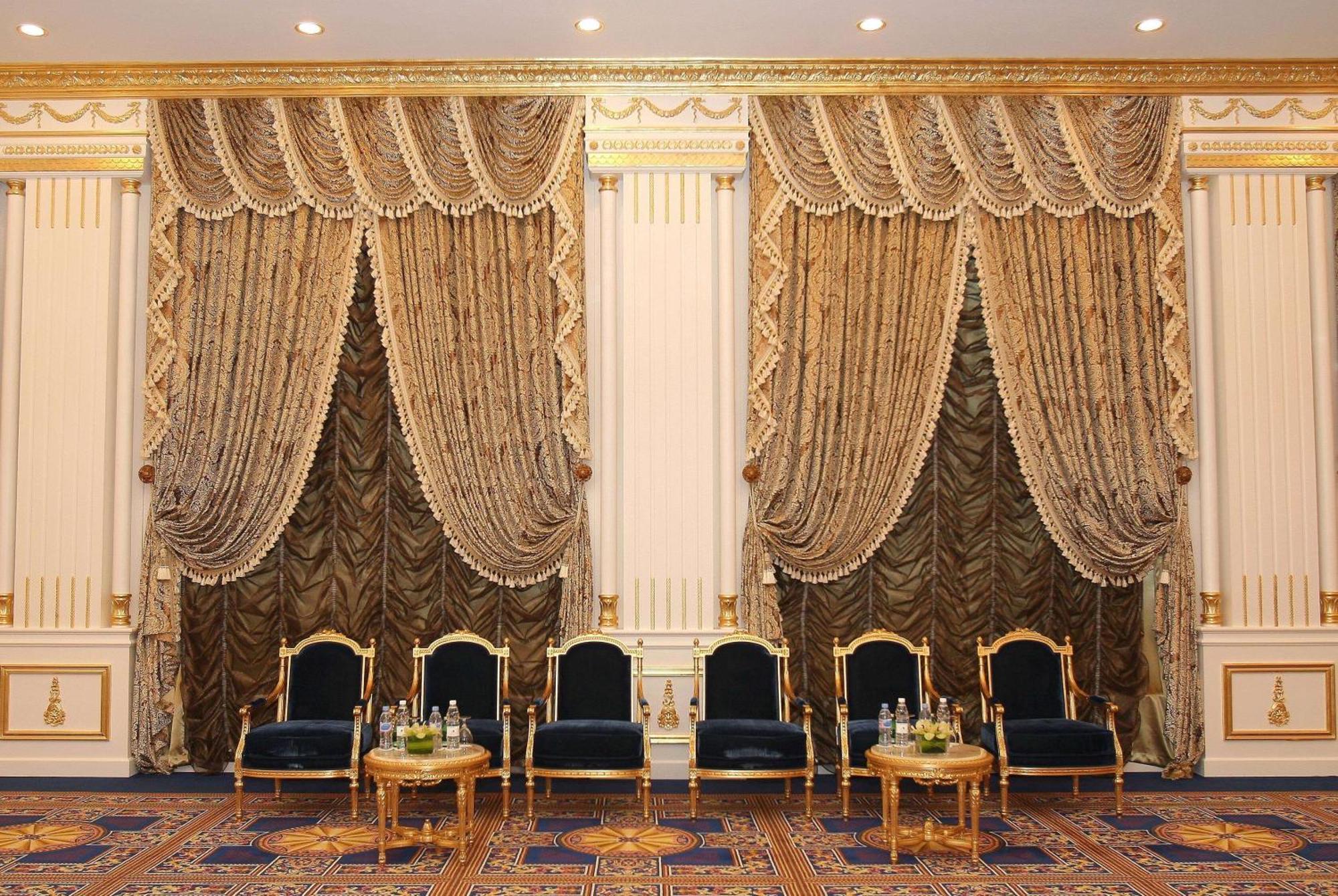 Grand Regency Doha, Trademark Collection By Wyndham Екстериор снимка The photo shows an elegantly decorated interior space. There are two sets of opulent curtains on the walls, featuring rich fabrics with ornate designs and gold accents. The curtains are paired with decorative tiebacks. In front of the curtains, there