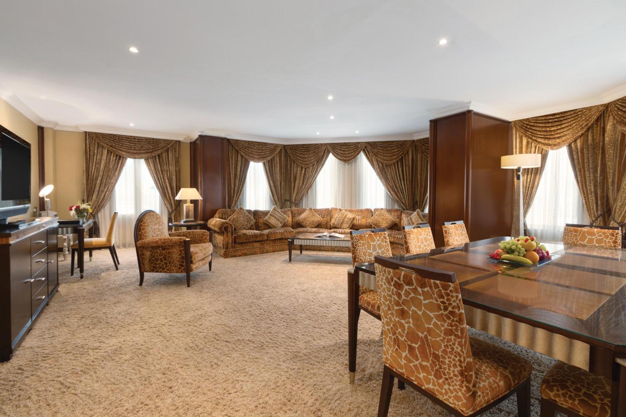 Grand Regency Doha, Trademark Collection By Wyndham Екстериор снимка The photo shows a spacious and elegantly designed living area. There are large windows dressed with luxurious curtains, allowing natural light to fill the room. The seating arrangement features a comfortable sofa with various cushions and several sty