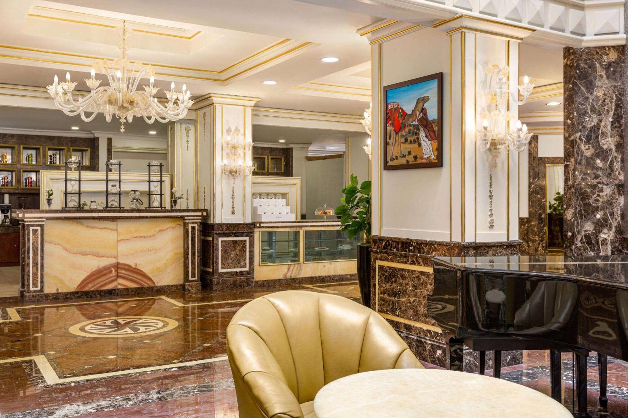 Grand Regency Doha, Trademark Collection By Wyndham Екстериор снимка The photo depicts an elegant hotel lobby interior. It features a polished marble floor with intricate patterns. In the background, there is a reception desk made of marble and wood, with decorative elements and a glass display. On the walls, you can 